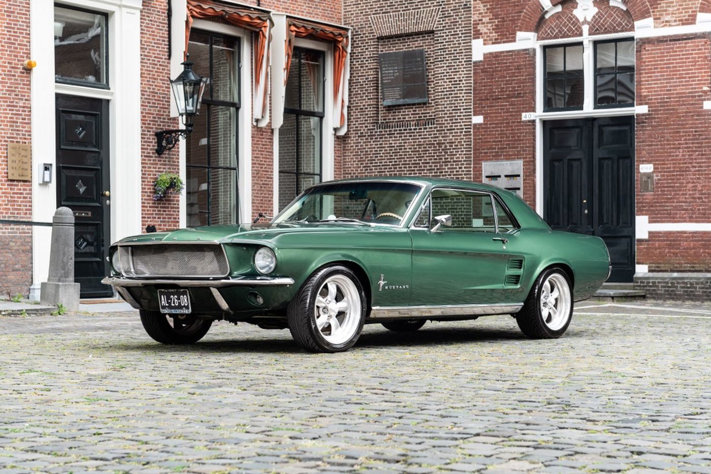 Groene Ford Mustang coupé op de keien voor een rij grachtenpanden — veiling