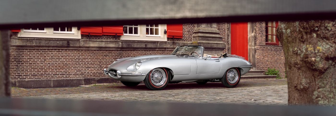 Zilvergrijze Jaguar E-type roadster voor een bakstenen gevel — auto verkopen